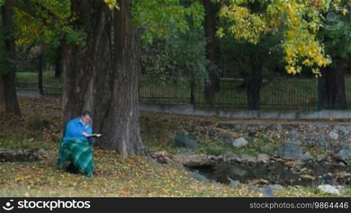 Senior woman enjoying her retirement in a chair under an autumn tree, reading a book.
