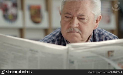 Seniors and active retirement, old man with mustache reading newspaper in library