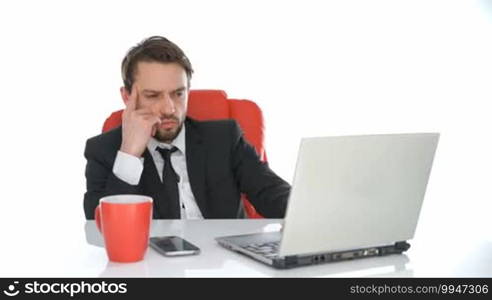 Serious businessman working at his laptop sitting at his desk reading information on the screen, close-up view over white