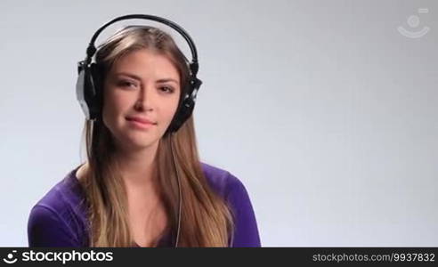 Sexy young woman listening to music playfully puckering up her lips and blowing a kiss at the camera on white. Expressive girl with a headset enjoying her favorite song on the radio and flirting with the camera.