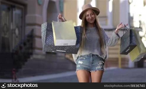 Shopaholic woman holding many shopping bags excited. Blond female showing paper bags with new clothing