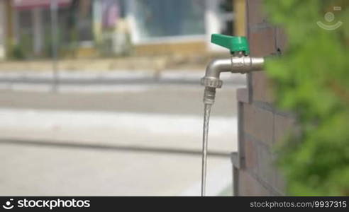 Shot of boy in straw hat and sunglasses washing his hands and refreshing himself in a fountain faucet in a public place on a summer day in Piraeus, Greece