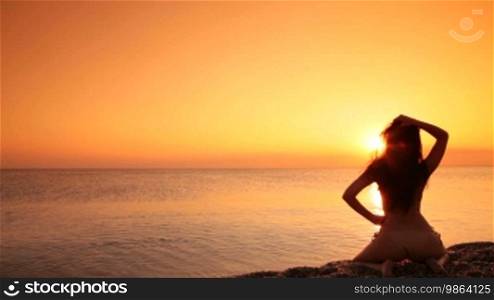 Silhouette of a woman sitting on a beach at sunset