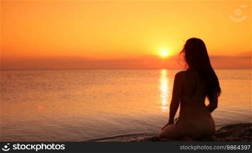 Silhouette of a woman sitting on a beach at sunset