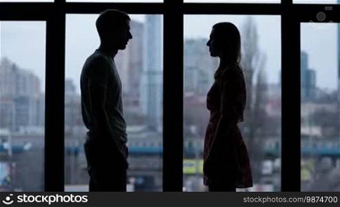 Silhouette of couple in love holding hands by window over cityscape background. Slow motion. Romantic couple bonding to each other.
