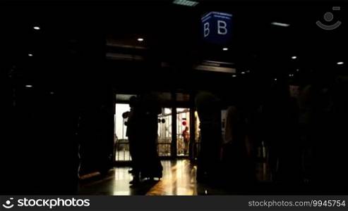 Silhouette of passengers in the airport carrying bags and luggage trolleys in the early morning with backlit sun rays going through the window