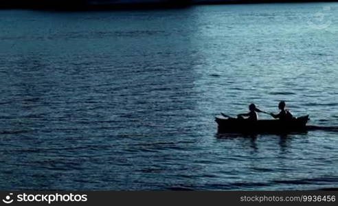 Silhouette of people kayaking in the sunset at the sea near the shore