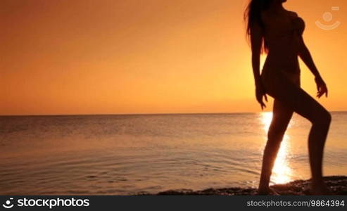 Silhouette of young woman in a bikini coming out of the sea at sunset