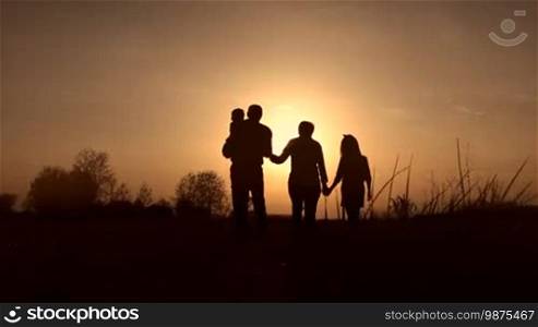 Silhouettes of loving grandparents with two kids walking in the meadow in the glowing of an amazing sunset in springtime. Multi-generation family with siblings enjoying a great time in the setting sun. Slow motion. Steadicam stabilized shot.