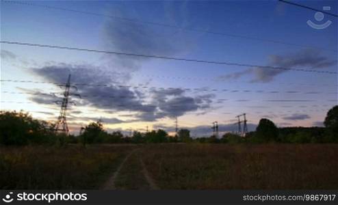 Silhouettes of powerlines in a flat landscape and setting sun. Timelapse.