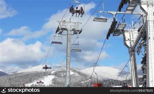 Ski lifts with skiers are moving over snow-covered mountains, bottom view, timelapse