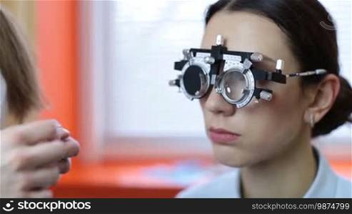 Skillful ophthalmologist with equipment for lens determination examining eyesight of female patient in ophthalmology clinic. Female optician determining prescription values with trial frame for stunning woman in oculist office closeup.