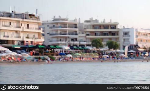 Slightly defocused shot of summer resort with crowded beach and people swimming in the sea, hotels in background. Vacation and tourism