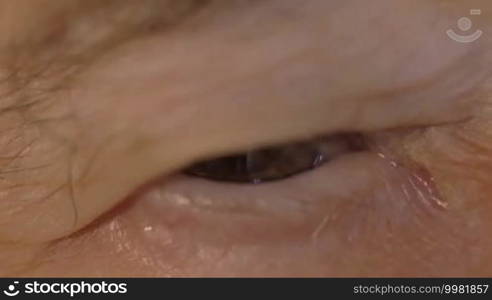 Slow motion and extreme close-up shot of a senior woman's eye looking at the camera. Tired look and wrinkled skin