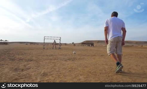 Slow motion and steadicam shot of a man kicking a goal during playing football in a resort area. Outdoor sports and activities