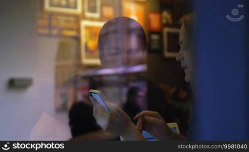 Slow motion clip of view through restaurant glass of woman and man discussing some topic, woman shows something on the smartphone and gesticulates