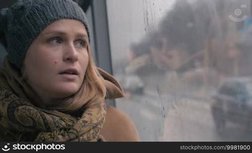 Slow motion close-up shot of a young sad woman traveling by bus on a dull rainy day. She looking out the wet window and breathing heavily. Loneliness in a big city