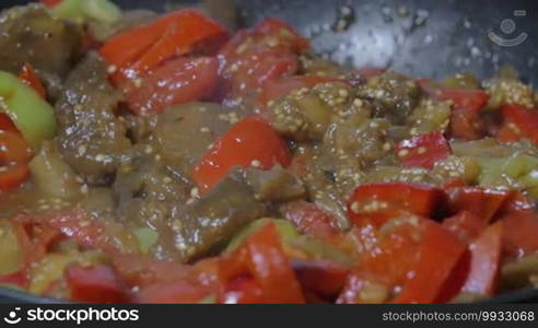 Slow motion close-up shot of pouring soy sauce into the frying pan with stewed vegetables. Cooking vegetarian dish