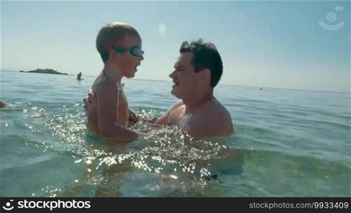 Slow motion of a father throwing son up from the sea. High fly from the water in dad's hands against bright shining sun. Happy summer holidays