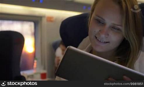 Slow motion of a happy young woman using a tablet computer for communication or entertainment during a train ride