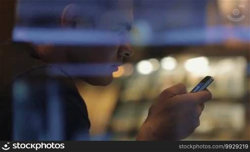 Slow motion of a man with a smartphone behind the glass in the evening. He is browsing a social network service on his mobile