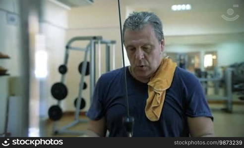 Slow motion of a mature man having a hard workout on a pull-down machine. Getting fit in a modern fitness center