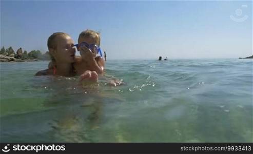 Slow motion of a mother and son bathing in the sea. She is holding the little boy in her arms and he is splashing water with his feet. The child has a playful and happy look.