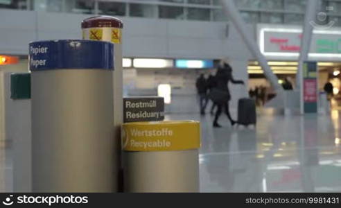 Slow motion of a woman coming up to the litter bins at the airport and throwing out a plastic bottle into a recyclable bin. Waste sorting