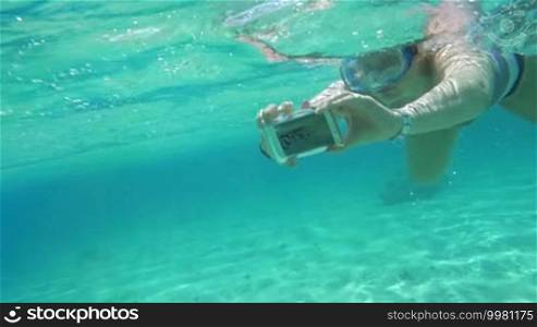 Slow motion of a woman in snorkel diving with a smartphone in a waterproof case. Making a selfie or taking pictures underwater