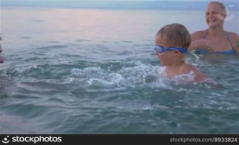 Slow motion of a young family with a little child having an enjoyable time in the sea. They are splashing water at each other and laughing. Happy vacation time