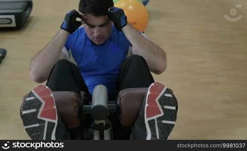 Slow motion of a young man doing sit-ups, exercising on special sports equipment in the gym