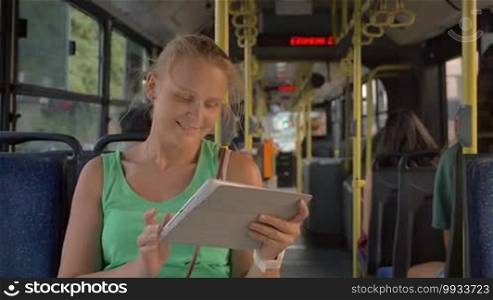 Slow motion of a young smiling woman using touch pad in the public transport. Bus cabin in the background