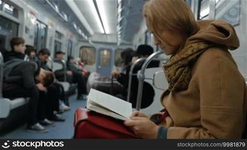 Slow motion of a young woman commuter reading a book in a moving metro train. Passing the time during everyday ride