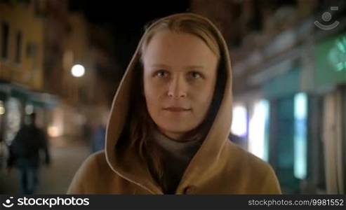 Slow motion of a young woman in coat and cowl walking in the city street in the evening