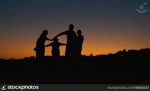 Slow motion of big family with child in a circle holding hands. Their black silhouettes against colorful evening sky
