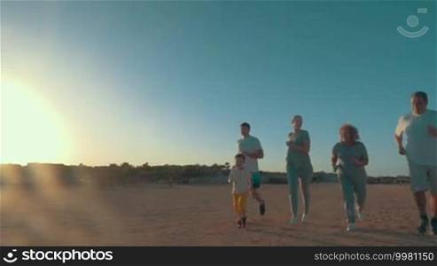 Slow motion of big family with little child jogging on the beach in bright evening sunlight. Sports activity on vacation