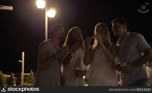 Slow motion of four happy friends taking a selfie with a smartphone in the street while they are out at night and drinking coffee