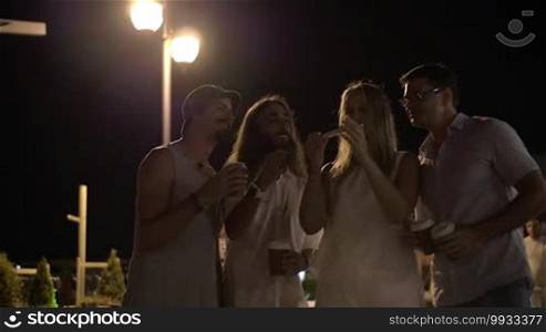 Slow motion of four happy friends taking a selfie with a smartphone in the street while they are out at night and drinking coffee