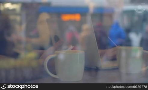 Slow motion of man and woman using smartphone and laptop while having tea in cafe. Reflection of city in the glass