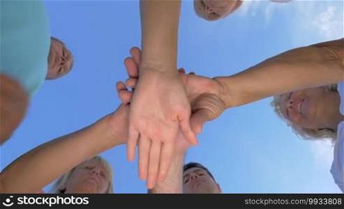 Slow motion of people making stack of hands on the background of clear blue sky, bottom shot. Unity and teamwork concept