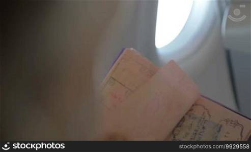 Slow motion shot of a hand turning pages of a travel passport with marks of entrance to different countries. Person is sitting in the plane.