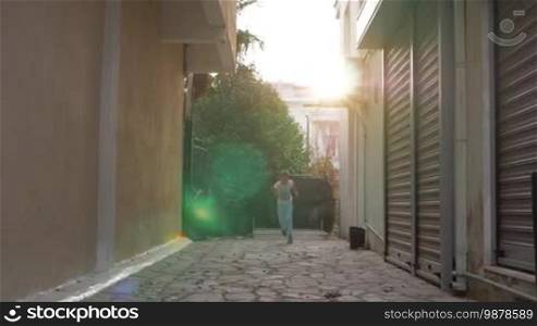 Slow motion shot of a happy and excited boy running along the paved alleyway. Shot with sun flare