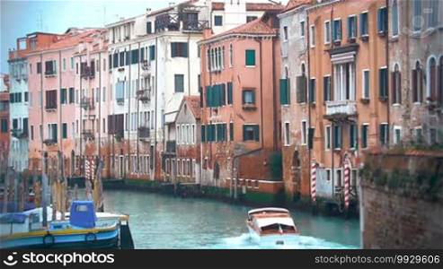 Slow motion shot of a motor boat sailing along the water canal beside ancient high-rise buildings in Venice, Italy.