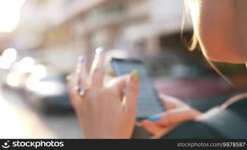 Slow motion shot of a woman using a cell phone in the street. She is checking new messages on social media