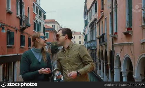 Slow motion shot of a young couple standing outdoors in Venice, Italy wearing Venetian carnival masks. They are kissing, smiling, and throwing confetti.