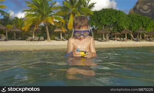 Slow motion shot of child in snorkel bathing in the sea with waterproof camera. He is searching for good underwater shots during vacation on a tropical resort