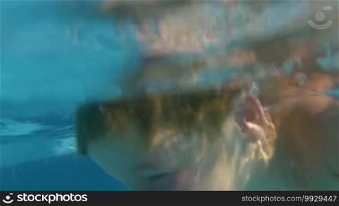 Slow motion shot of parents and son diving in swimming pool and playing underwater.