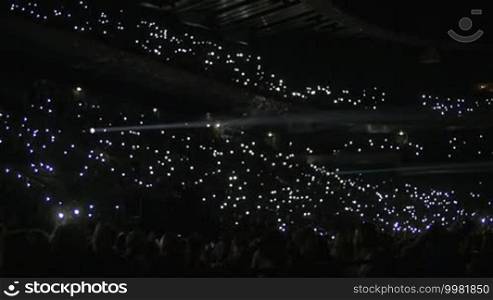 Slow motion shot of stadium stand full with people. They are lighting lamps in the dark.