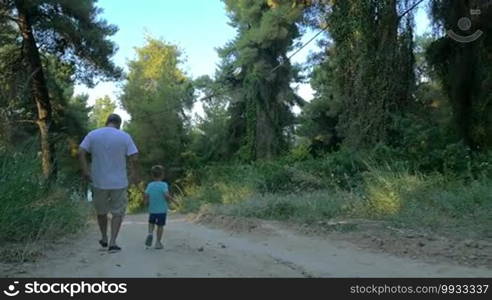 Slow motion steadicam shot of a grandfather and little grandson running down the road in the woods, back view