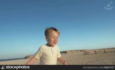 Slow motion steadicam shot of a happy little boy running on the beach and meeting his dear father who is picking him up
